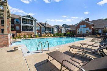 A pool surrounded by lounge chairs and buildings in the background.